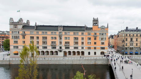 View of Rosenbad from the West Wing of the Riksdag. Greenery in the foreground and people crossing the bridge.