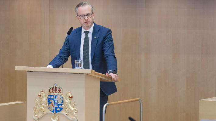Mikael Damberg (Social Democratic Party) stands at the rostrum which is decorated with the national coat of arms. 