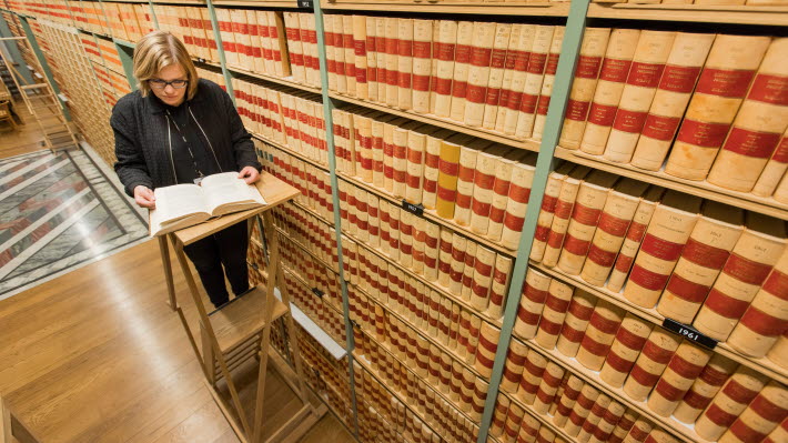 Bibliotekarie Lotta Åberg Brorsson läser ur riksdagstrycket. Bild tagen uppifrån. I bakgrunden syns riksdagstrycket.