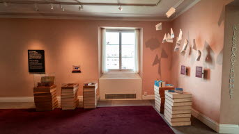 Bild på ena sidan av rummet med papper i taket som hänger ner från små trådar och boktravar i trä under.