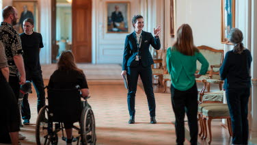 Guide visar besökare i Sammanbindingsbanan. Ryggar på människor syns varav en person i rullstol.